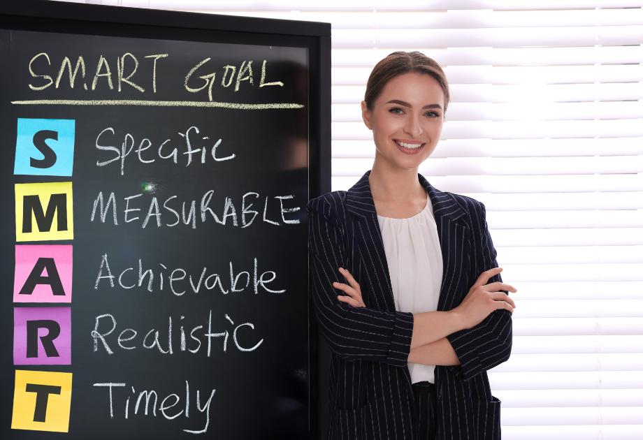 a woman leaning against chalkboard that says" Smart Goal"